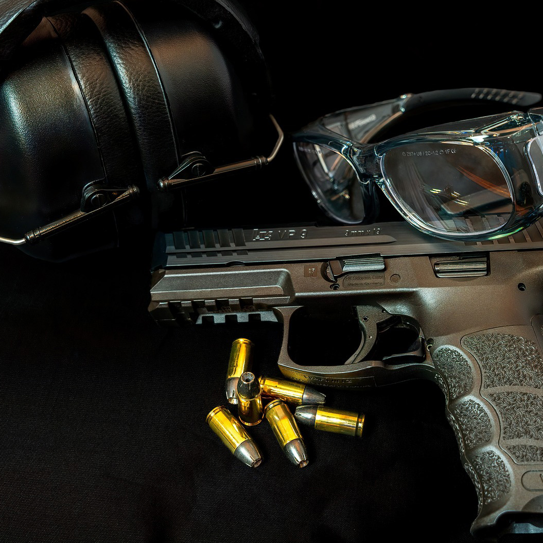 A close-up image of a handgun, some ammunition, safety glasses and a pair of earmuffs
